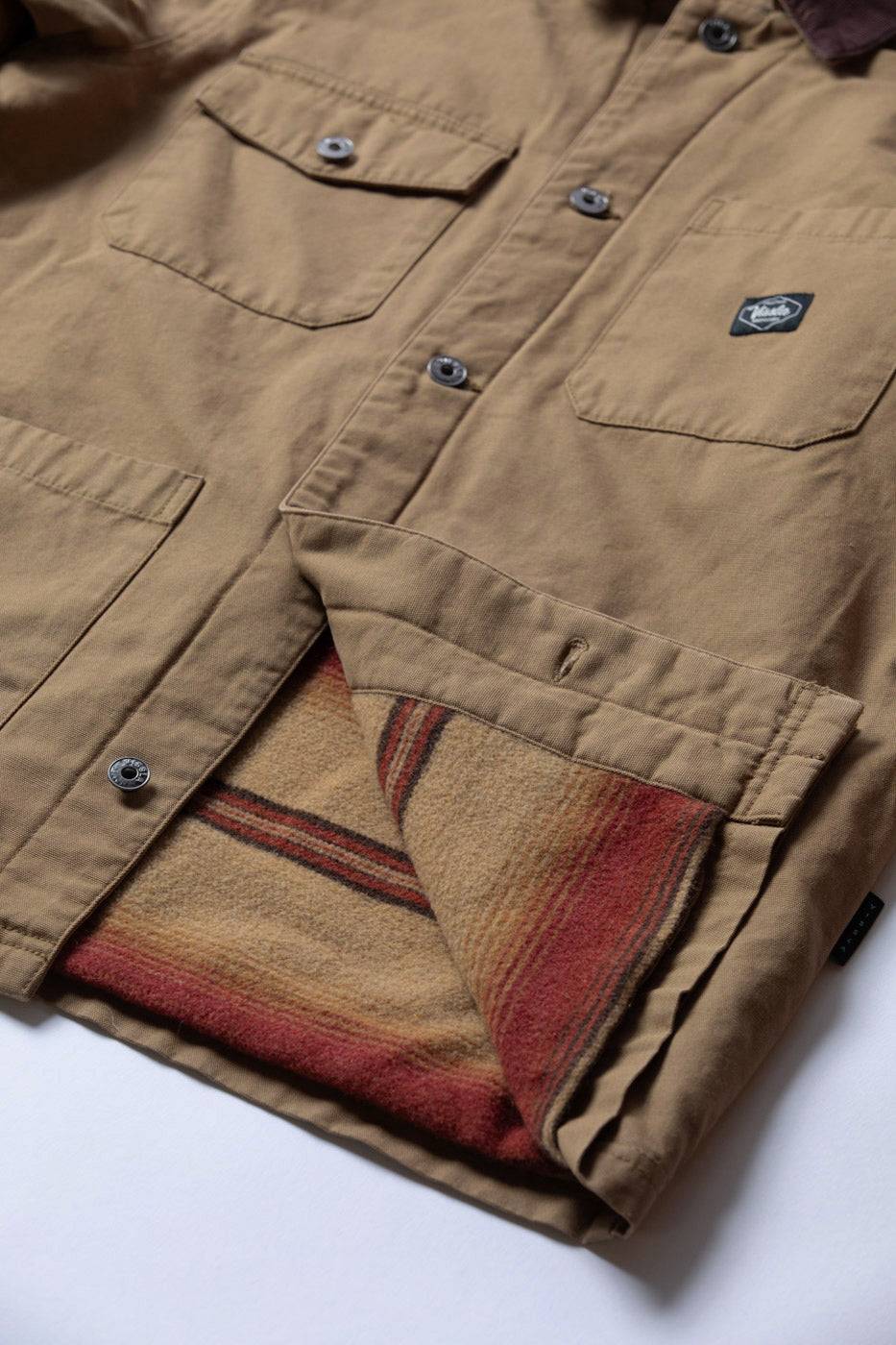 Vissla Peterson Jacket in tan cotton canvas with buttoned chest pockets, dark collar and striped red and beige lining