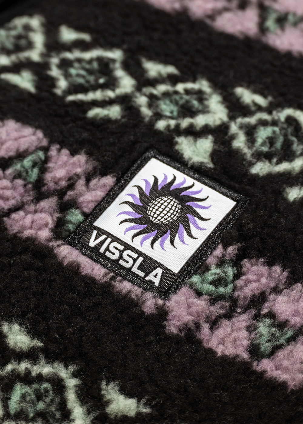 Vissla Hiking Ice sherpa fleece pullover in black with lavender and mint geometric pattern and woven chest logo patch.