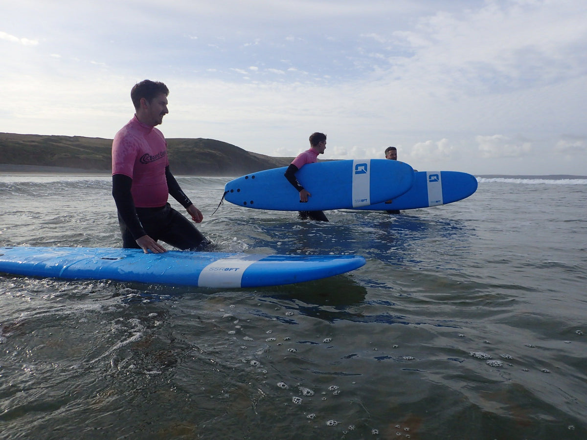 7ft x 25in Beginner Surf School softboard, bright blue with white panels, black leash plugs and rounded nose.