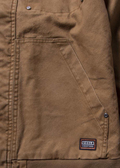 Vissla Creators Grit Jacket in brown cotton canvas, featuring a large angled pocket, metal snaps, and logo patch.