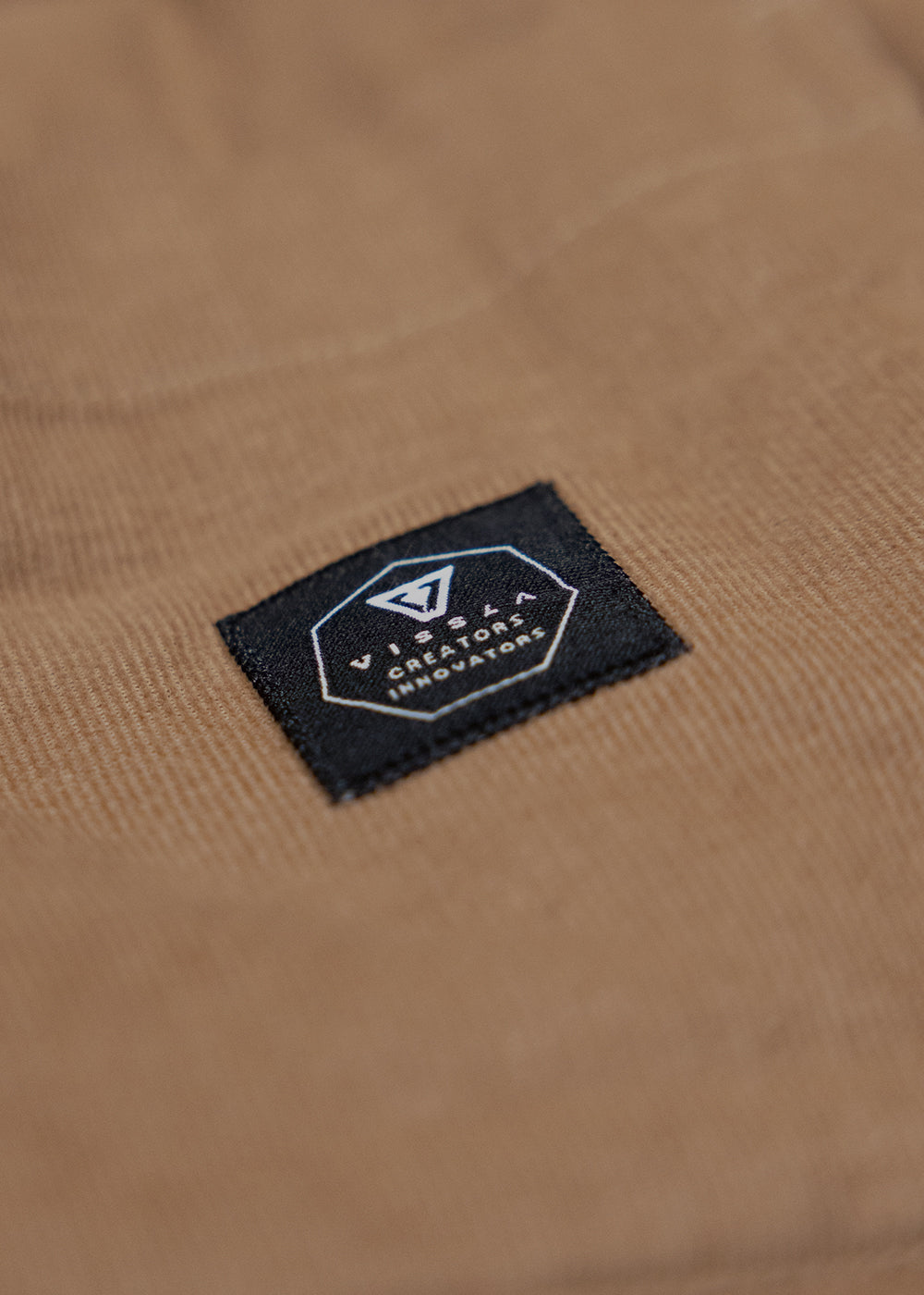 Vissla Paxon Jacket in tan corduroy, featuring a black rectangular brand patch with white logo embroidery.